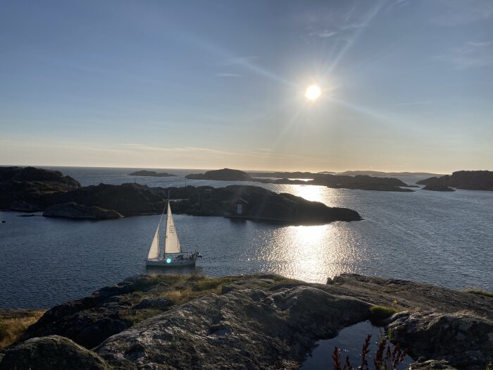 Segelbåt på en solbelyst fjord med klippöar i bakgrunden under en klar himmel med solnedgång.