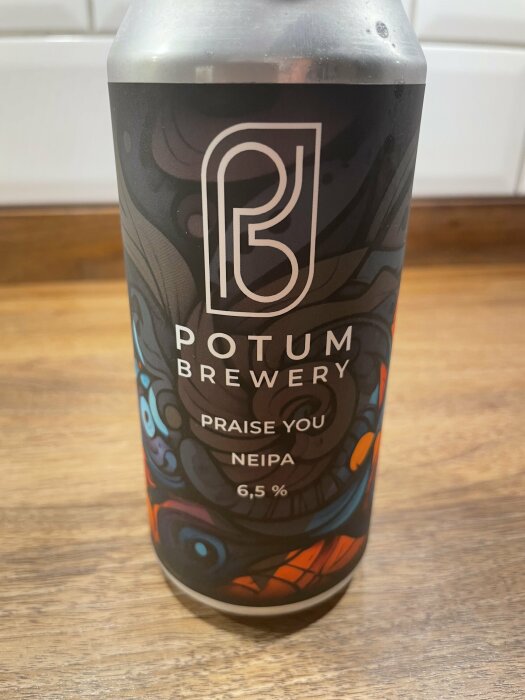 Burk med Potum Brewerys öl "Praise You NEIPA" på ett träbord, 6,5 % alkoholhalt.