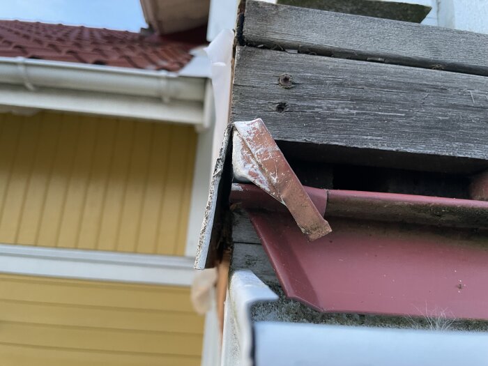 Plåtskiva och träpanel på hus med fuktskadad träbalk och planka synlig under plåtblecket.