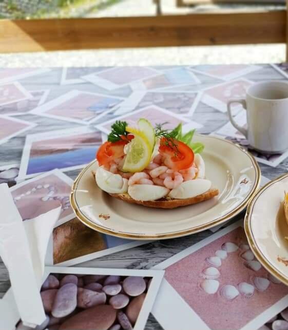 XL-räksmörgås med ägg, tomatskivor, citronklyfta och dill, serverad på ett porslinsfat på ett bord inomhus. En kopp syns i bakgrunden.