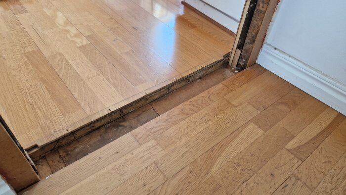 Stort hål i golvet där den gamla tröskeln suttit, omgiven av parkettgolv i äldre del av huset under byte av dörrkarm.