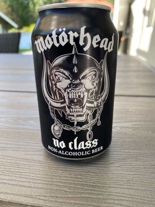 En burk alkoholfri öl med Motörhead-märke och texten "No Class" på ett bord, med en uteplats i bakgrunden.