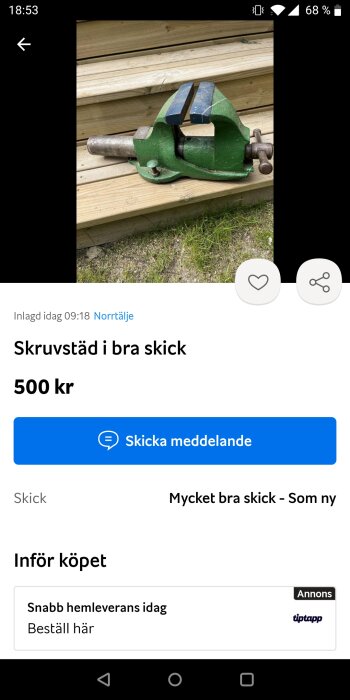 Grönt skruvstäd i metall med blå käftar, placerat på en trappa av trä.