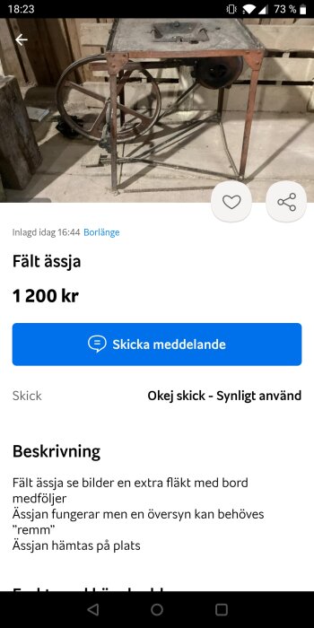 En fältässja till salu med en handdriven vev, stativ och uttag för fläkt. Bakgrunden visar en trävägg och golv, samt bruksföremål runtomkring.