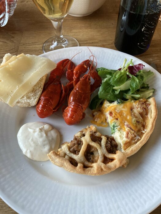 Tallrik med kräftor, sallad, paj, bröd med ost och en klick sås. I bakgrunden syns ett glas dryck och en flaska Coca-Cola.