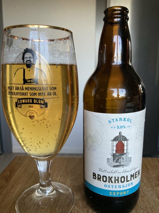 Ett glas öl med etikett som säger "Edward Blom" och en ölflaska med etikett "Brokholmen Östersjön Export", ståendes på ett träbord.