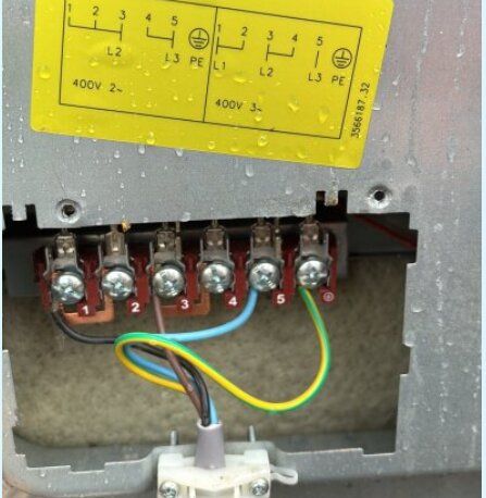 Närbild av en tre-fas elektrisk anslutning med fem numrerade terminaler och kopplingskablar i olika färger. Över terminalerna finns ett kopplingsschema.