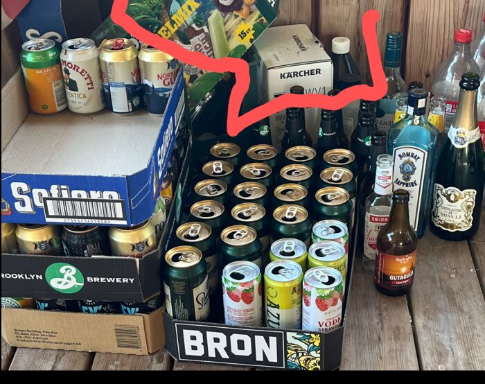 Flera backar med ölburkar och spritflaskor på en träyta, inklusive märken som Sofiero, Brooklyn Brewery och Bombay Sapphire.