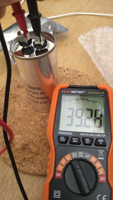 En digital multimeter mäter kapacitansen hos en nyinstallerad kondensator, med läsning på skärmen som visar 39,28 uF.