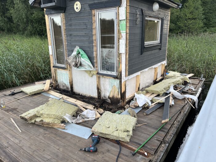 Bastuflotte under renovering, med trallgolv och väggar borttagna för att åtgärda rötskador. Isoleringsmaterial och verktyg ligger på golvet.