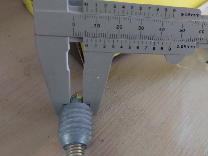 En karmskruv mäts med skjutmått som visar ett mått på 6 mm på sexkanten, ligger på en trädskiva.