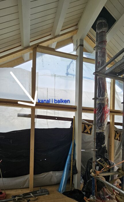 Byggprojekt av ett åretrunt uterum med träbalk där en kanal för belysning är markerad. Plastskyddade delar och verktyg finns i bakgrunden.
