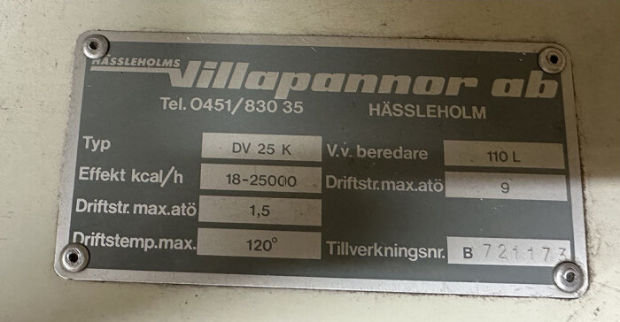 Skylt på värmepannan med texten "Hässleholms Villapannor ab, Hässleholm, Tel. 0451/830 35, Typ DV 25 K, V.v. beredare 110 L, Effekt kcal/h 18-25000, samt tillverkningsnr B721173".