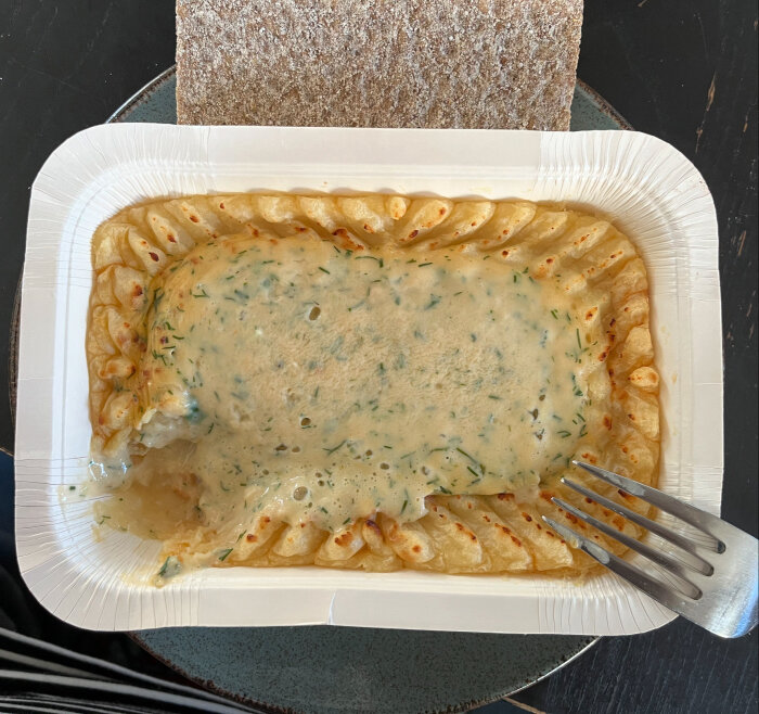 En förpackning med fiskgratäng, innehållande synliga räkor, kombinerat med en bit knäckebröd som lunchmåltid.