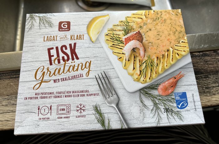 Förpackning av Gratäng Fiskgratäng med Skaldjurssås från Garant, med en bild på gratängen som innehåller fisk, räkor, potatismos och dillkvistar.