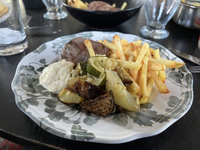 En tallrik med en bit grillat oxfilékött, pommes frites, ugnsstekta grönsaker och en klick bearnaisesås.