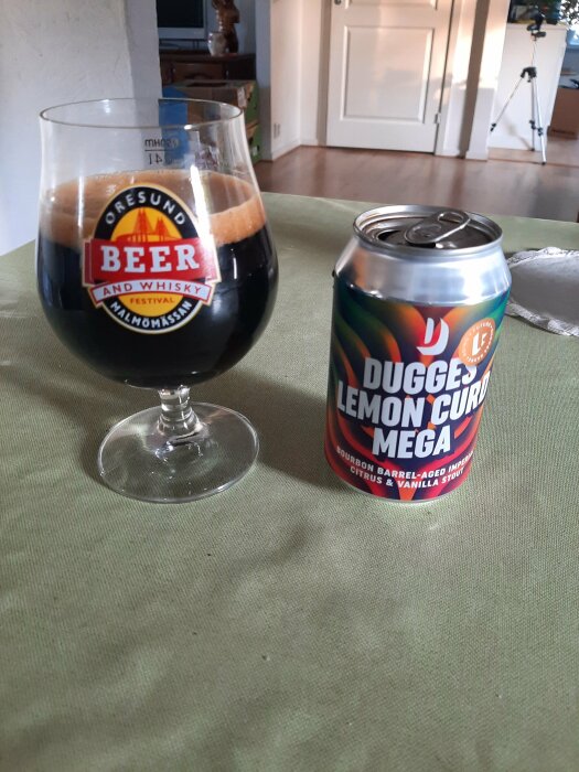 Ett ölglas med mörk stout från Öresund Beer and Whisky Festival bredvid en burk Dugges Lemon Curd Mega-stout på ett bord i ett vardagsrum.