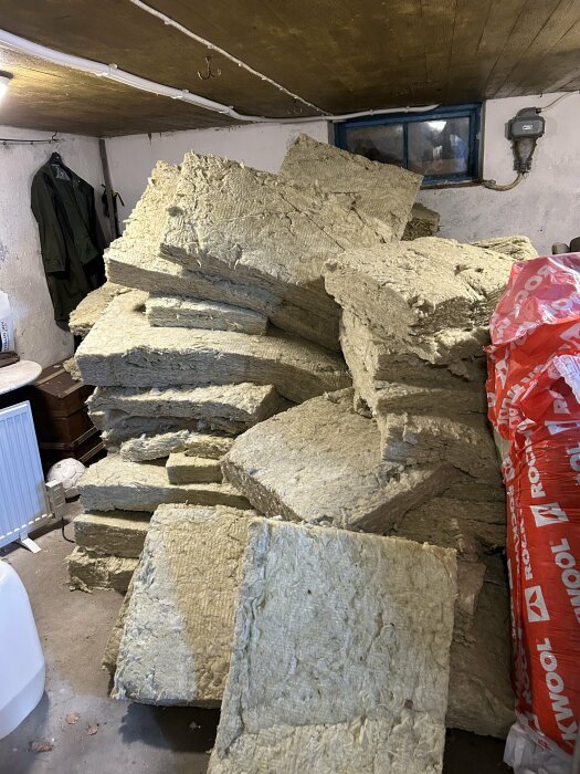 Staplar med isoleringsmaterial i ett sommarhus. Isoleringsplattorna ligger huller om buller bredvid en röd förpackning med märket Rockwool.