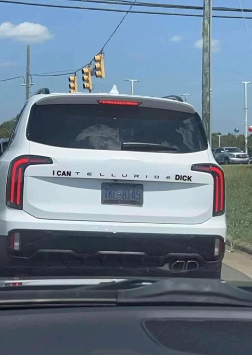 Vit SUV med ändrad märkning på bakluckan som nu lyder "I can Telluride dick". North Carolina registreringsskylt TKC-8125. Trafikljus i bakgrunden.