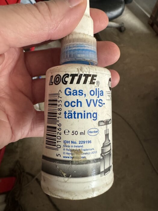 Hand som håller en flaska Loctite tätning för gas, olja och VVS, 50 ml, märkt Henkel. Flaskans etikett är delvis sliten.