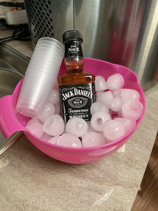 Jack Daniels-flaska i en rosa skål med isbitar och plastmuggar.