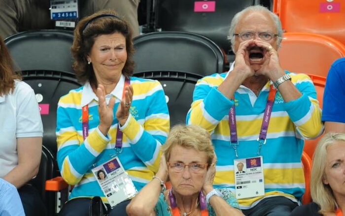 Personer klädda i svenska landslagströjor visar olika reaktioner på VIP-läktaren under en handbollsmatch på OS 2012 i London.