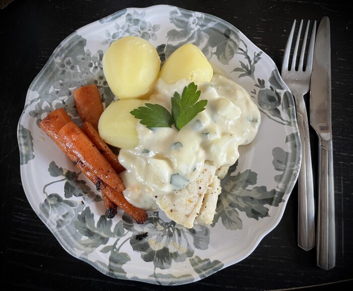 En tallrik med kokt torsk, ägg- och persiljesås, kokt potatis, smörstekta morötter och ett persiljeblad som dekoration.