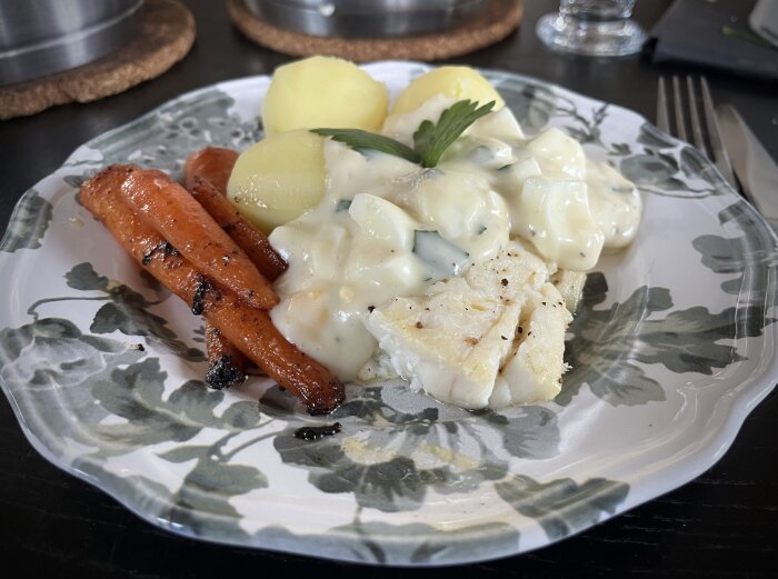 En tallrik med torskrygg, ägg- och persiljesås, kokt potatis och smörstekta morötter, garnerad med bladpersilja.