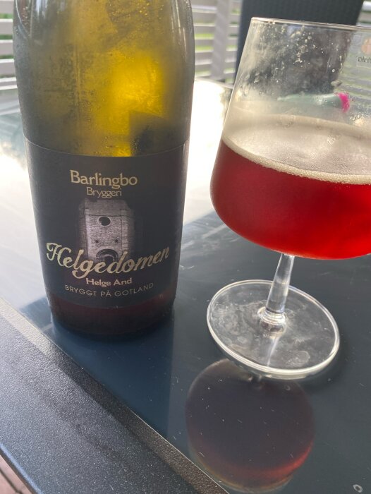 En flaska Belgiansk stil öl från Barlingbo Bryggeri bredvid ett glas med mörk öl, placerade på ett bord.