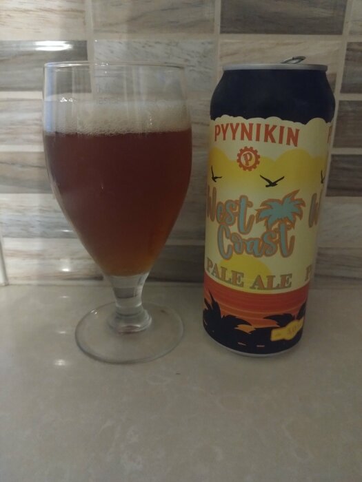 En glas öl bredvid en burk Pyynikin West Coast Pale Ale på en köksbänk.