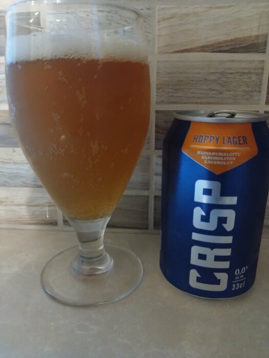 Ett glas med gyllene öl bredvid en blå burk med texten "Hoppy Lager" och "CRISP".