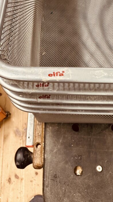 Fyra Elfa meshbackar staplade på varandra, står på en arbetsbänk av trä och metall, varumärket "elfa" synligt på framkanten av varje back.