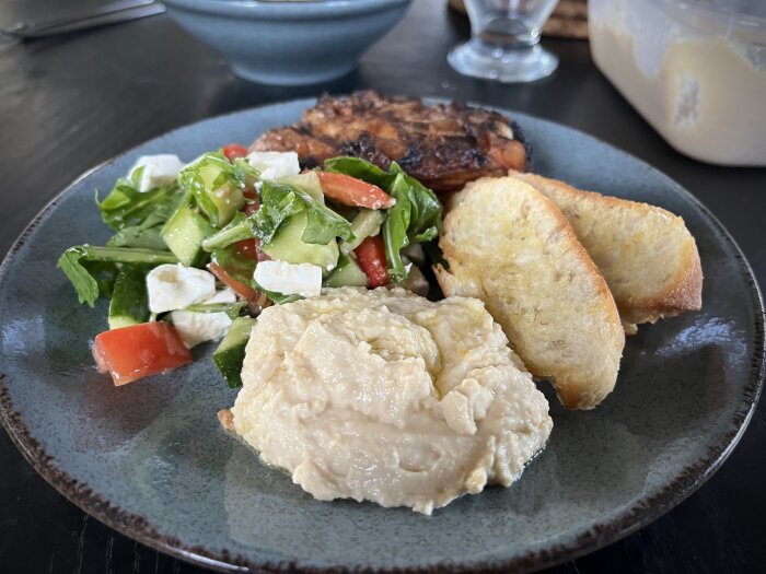 En tallrik med sallad, hummus, crostini och ett kycklingben.