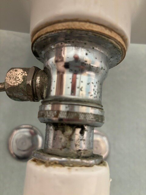 Närbild på en vattenlåsanslutning till ett tvättställ, med synligt rör och muttrar, där det verkar vara kalkavlagringar och korrosion.