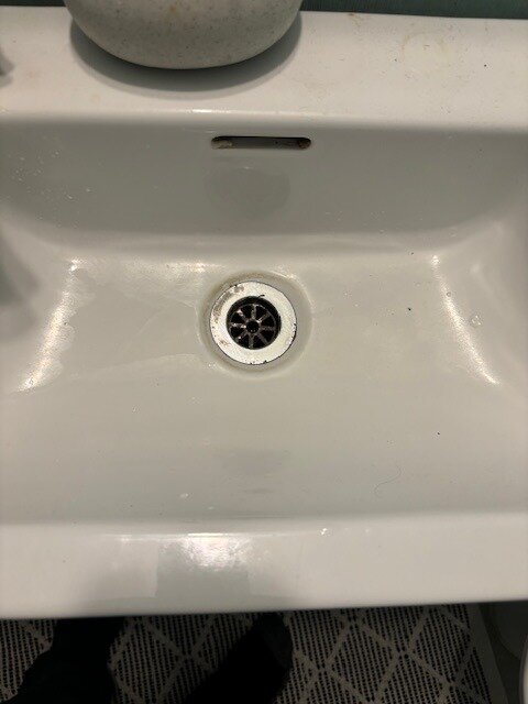 Ett tvättställ med avloppshål och synlig bottenventil, sett ovanifrån. Inga synliga gängor eller skruvar kring avloppet.