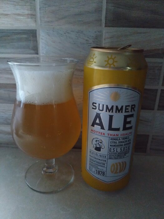 Ett glas öl bredvid en burk Olvi Summer Ale, marknadsfört som "Hotter than Iisalmi".