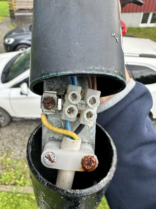 Närbild på en öppen lampa eller annan elektrisk enhet med kablar och skruvar, samt synliga rostiga skruvar inuti en metallhölje.