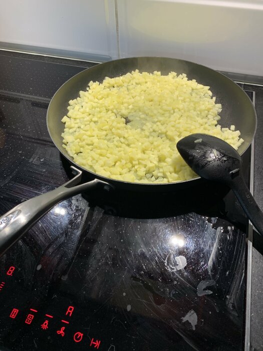 Diced potatoes being cooked in a large frying pan on a stovetop.