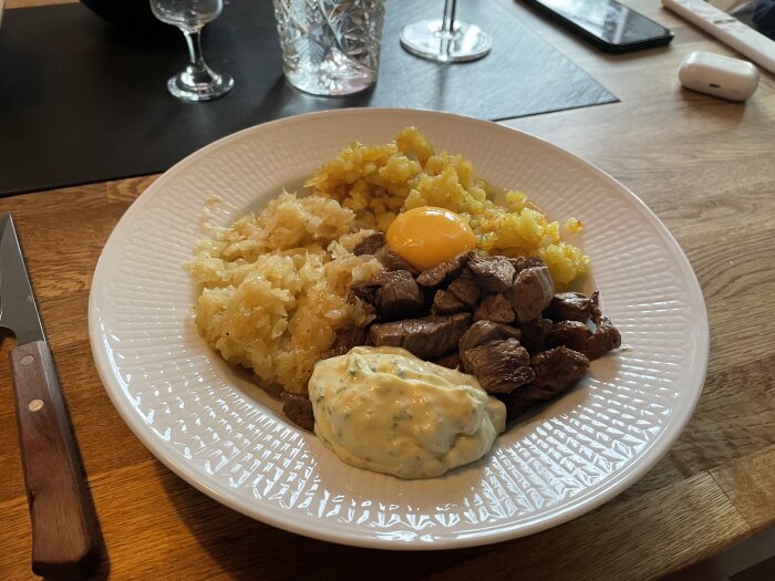 En tallrik med Biff Rydberg serverad med köttbitar, krossad potatis, rå äggula och lök tillsammans med en krämig sås.