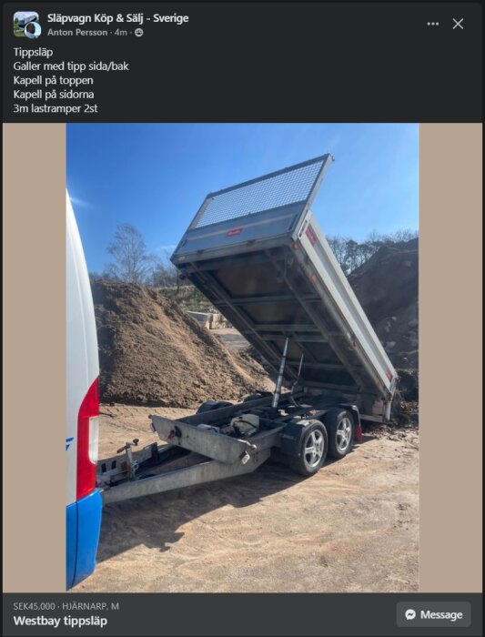 Westbay tippsläp i metall med tippfunktion bakåt, kapell på toppen och sidor, galler på sidorna, två lastramper och står framför en hög med sand.