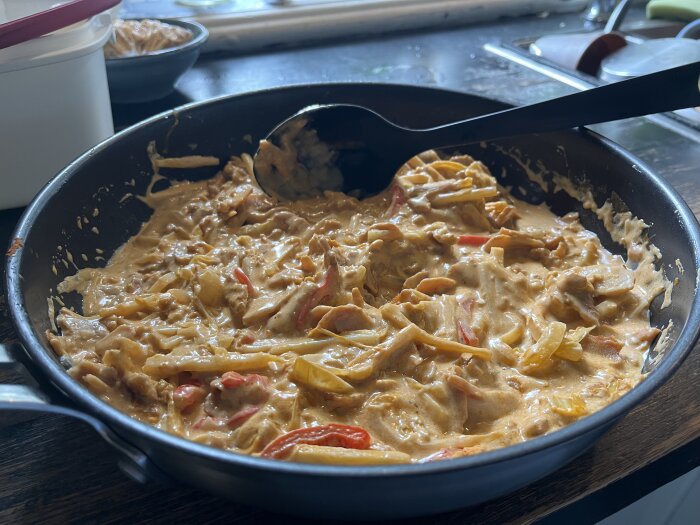 Kycklingrätt i en stekpanna med en krämig sås, innehållandes strimlad vitkål, paprika, bambuskott och kryddor, tillagad med thaimatsinspirerade smaker.