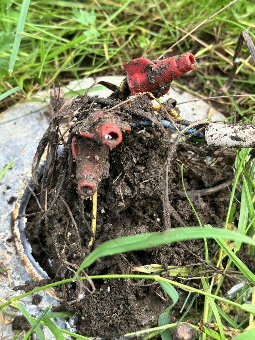 Närbild på smälta och brända elkablar och kontakter i marken omslutna av jord och omgeven av gräs.