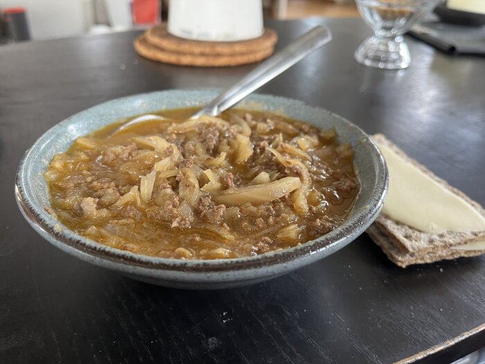 En tallrik med köttfärssoppa, troligen Nikkoluoktasoppa, serverad med en ostmacka på ett mörkt bord.