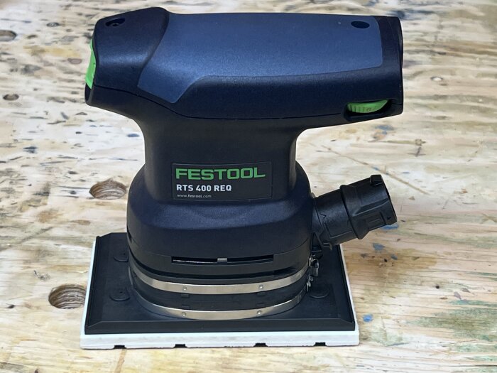 Svart och grön Festool RTS 400 REQ slipmaskin placerad på en trädbräda med borrhål.