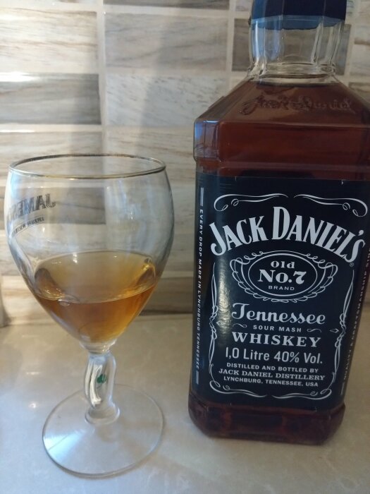 En flaska Jack Daniel's Tennessee Whiskey bredvid ett whiskyglas med en liten mängd whisky.