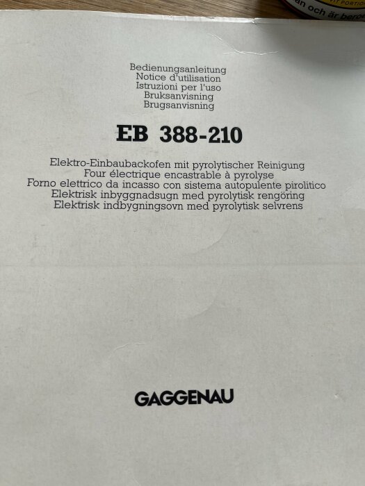 Bruksanvisning för Gaggenau EB 388-210, en elektrisk inbyggnadsugn med pyrolytisk rengöring, visas på flera språk på bänkskiva.