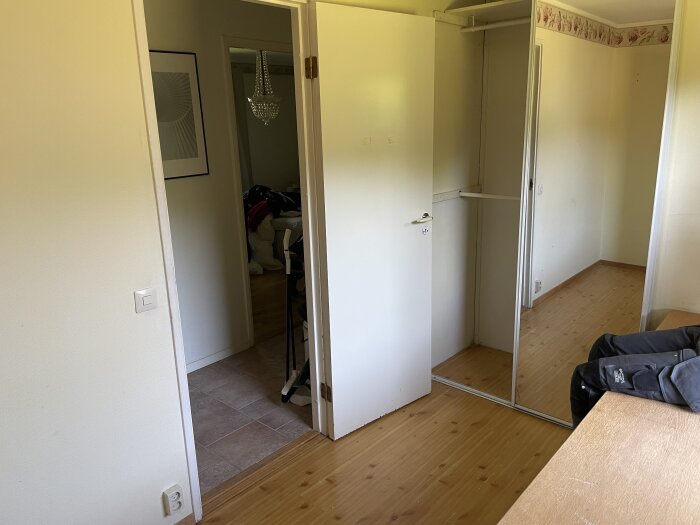 Ett sovrum under renovering med en dörr som öppnas in i rummet, en garderob med skjutdörrar och ett öppet utrymme framför.