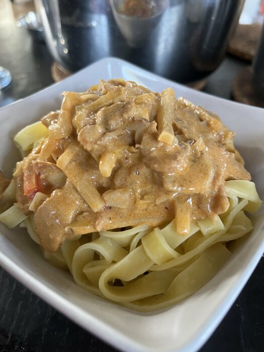 En skål med färsk pasta och en currysås med strimlade ingredienser serverad i närbild.