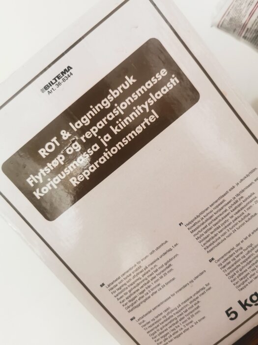 Förpackning av Biltemas reparationsmørtel märkt "ROT & laginsbruk" med instruktioner på svenska, norska, finska och danska, samt en vikt på 5 kg.