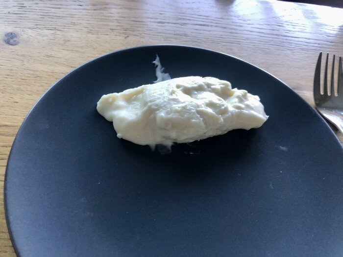 En bit krämig Gorgonzolaost på en svart tallrik på ett träbord, med en gaffel bredvid tallriken.